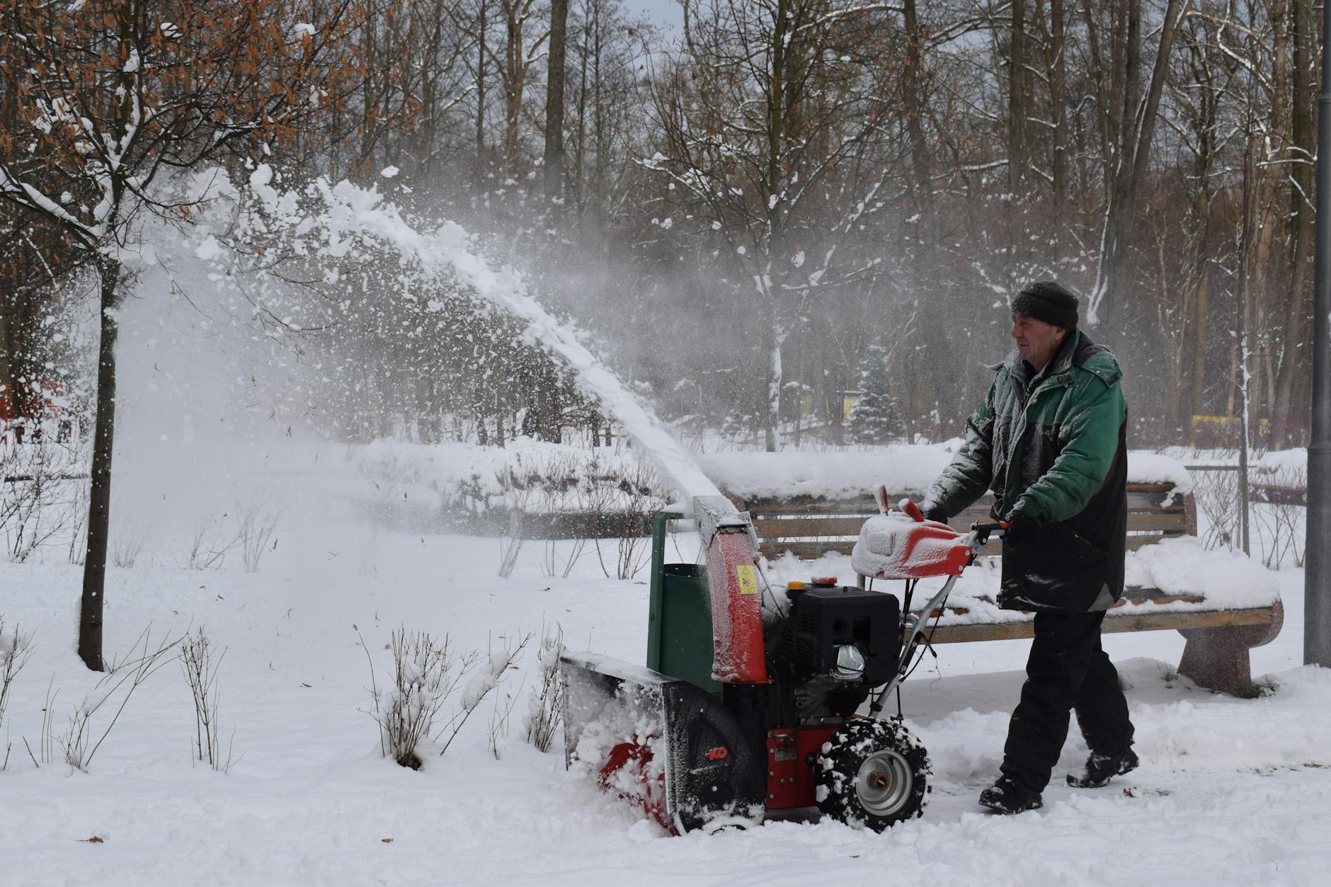 man in green jacket using snow blower